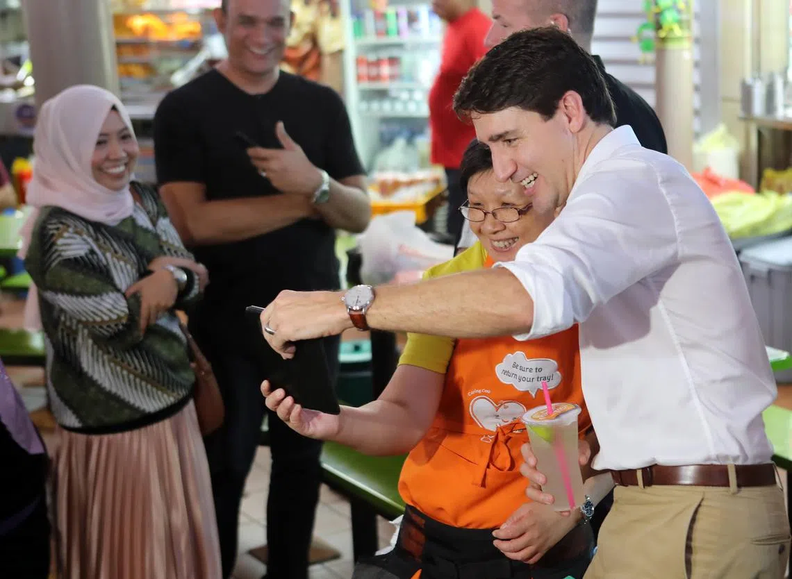 特鲁多总理（右一）在亚当路熟食中心与摊贩和食客亲切互动与拍照，完全没有“大人物”的架子。（联合早报）