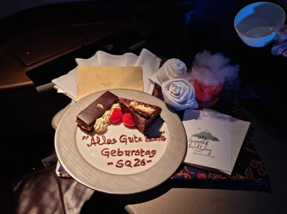 盘子上以德文写着“生日快乐”和航班编号（SQ26），这份蛋糕相信是为一名德国籍乘客准备。