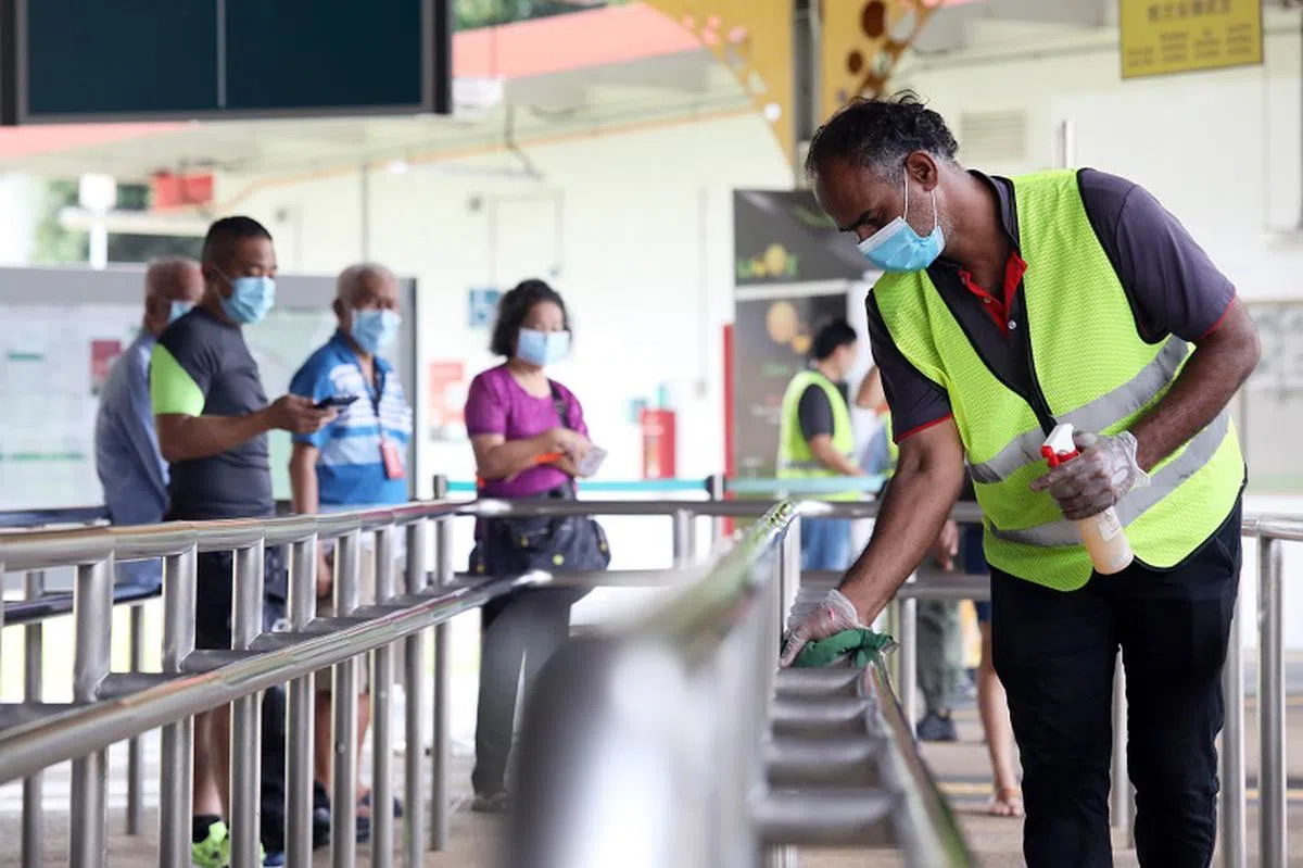 工人在消毒巴士总站的扶手。（联合早报）