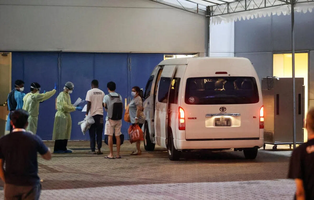  一群相信是轻症病患的人晚上乘坐迷你巴士送抵新加坡博览中心，在场工作人员为他们办理手续。（联合早报） 