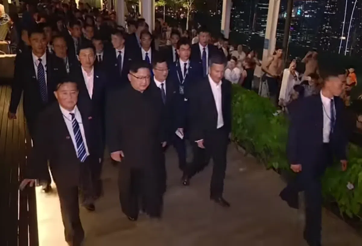  金正恩经过金沙酒店楼顶无边泳池，引起一阵骚动。照片右后方有位赤裸上身的老外游客跟着金委员长走。（朝鲜中央电视台纪录片截图） 