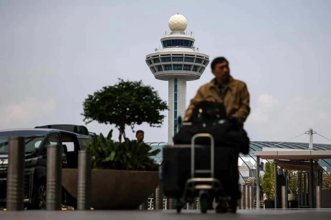 一名旅客推着行李，图后方为樟宜机场控制塔。(联合早报）