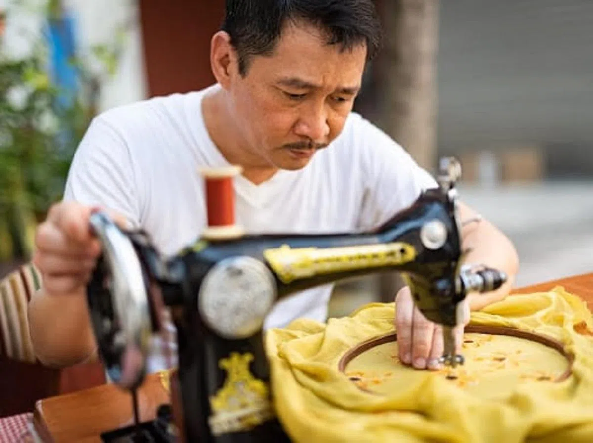 杨福来仍坚持以脚踩手动的传统针车缝制卡峇雅刺绣。（海峡时报）