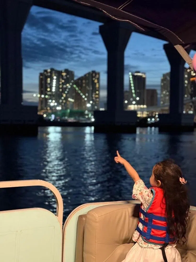 新山市区霓虹闪烁，远处的新加坡边境在夜色中若隐若现。游船还会经过正在建设的柔新捷运大桥下方。