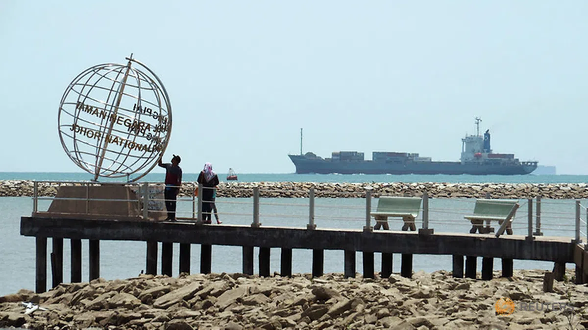  游人站在柔佛最南端看着一艘货船进入新加坡海峡。（路透社） 