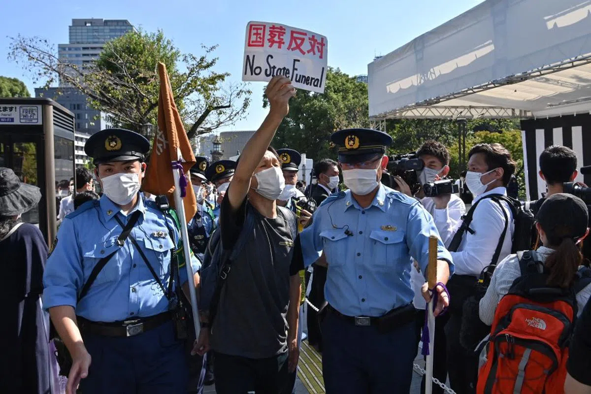 一名抗议国葬的民众在武道馆附近，人们排队献花的地点举起抗议标语，被警员带走。（法新社）