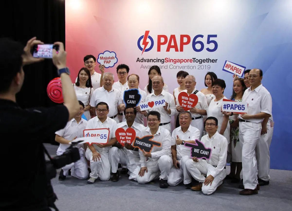  2019年，为庆祝行动党创党65周年，许多党工在大会场外，拿着各种标语合照留念。（联合早报） 