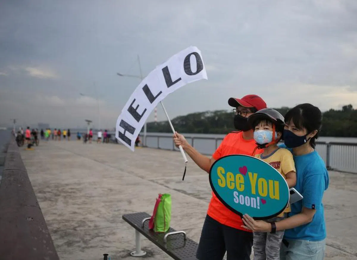  在兀兰滨海公园码头的公众手里拿着巨大的告示牌，好让船上家人能从人群中找到他们的身影。（联合早报） 