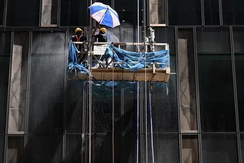 在高空中顶着太阳工作的客工，不得不用雨伞遮阳。（海峡时报）