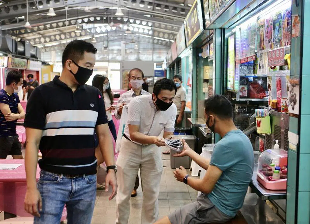  谢世儒（中）在蔡瑞隆（左）陪同下向亚历山大村熟食中心的小贩派发口罩。（联合早报） 