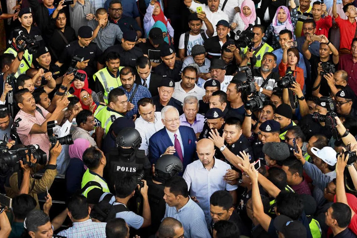 马来西亚前首相纳吉（中间打领带、戴眼镜）今天下午交保之后离开高庭时，被支持者和记者们里三层、外三层包围。（法新社）