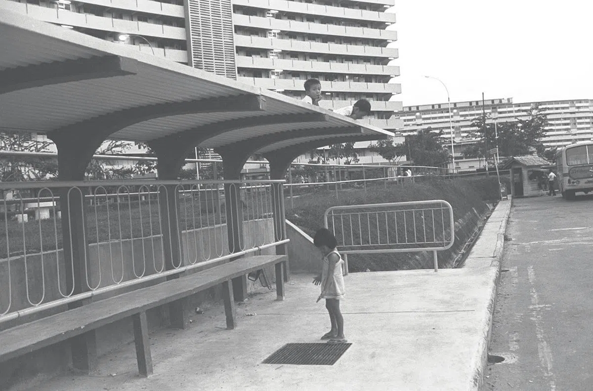 70年代，巴士站候车亭少了前面的护栏，后方的铁栏对照片里的两名男童来说，却更像是通往顶盖的路径。（海峡时报）