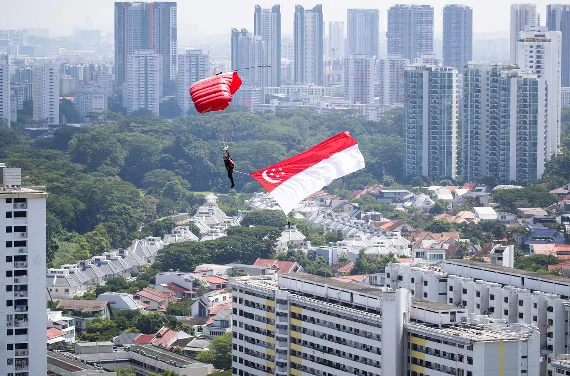 红狮跳伞队挂着新加坡国旗降落在政府组屋区。（联合早报）