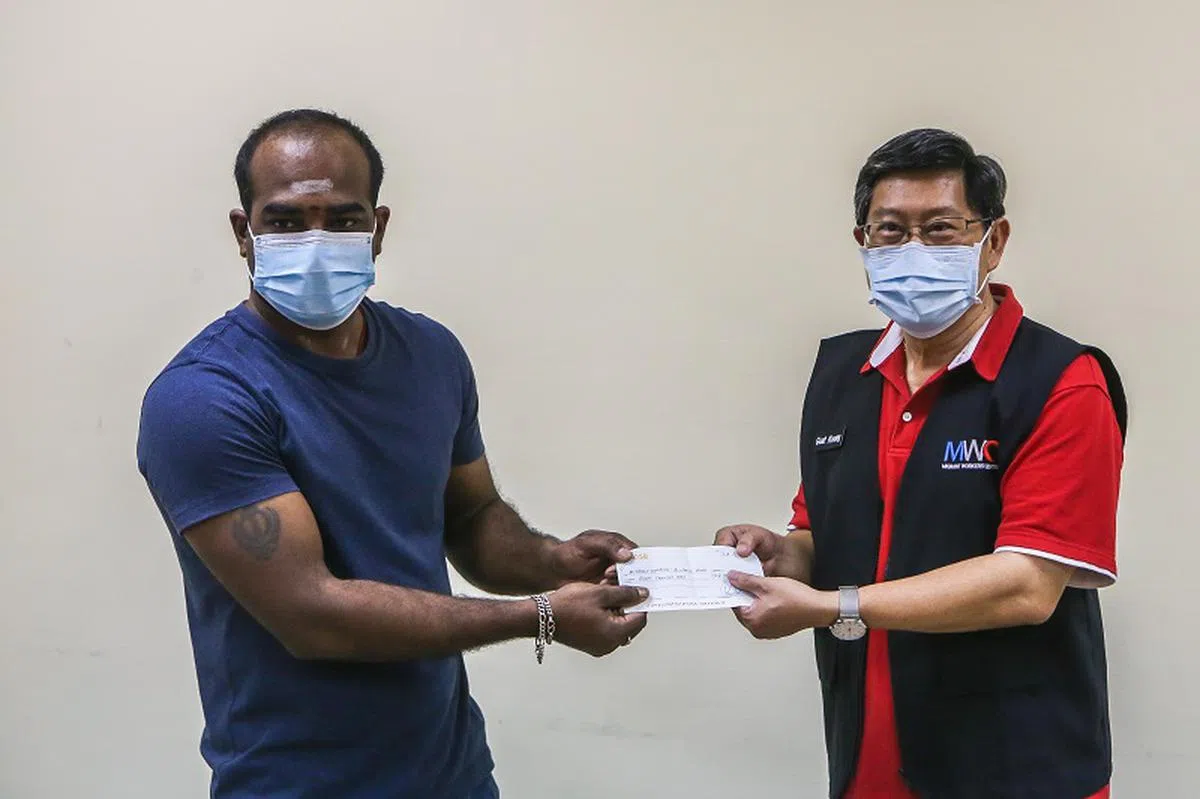  阿尼尔（左）在淡滨尼宿舍内把匿名善心人士的捐款支票交给外籍劳工中心主席杨木光。（联合早报） 