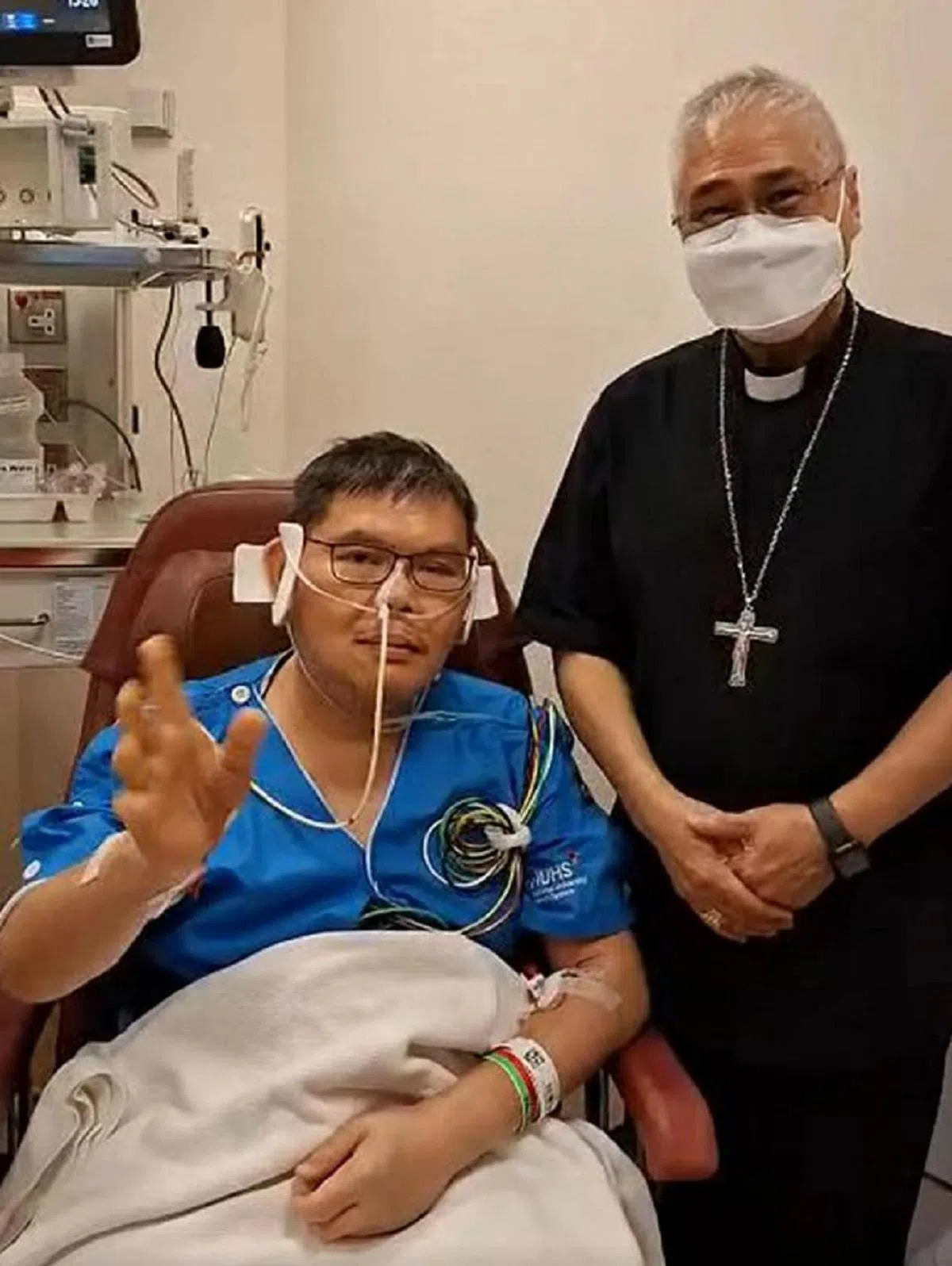 遇袭的李光兴神父（左）在天主教新加坡总教区总主教吴诚才的陪同下，在医院通过视频向信徒报平安。（吴诚才主教脸书截图）
