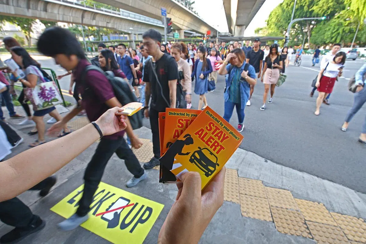 宏茂桥地铁站外交通灯前的地面上出现显眼的标志，提醒人们走路时“抬头看”，别成为边看手机边过马路的“低头族”。基层组织义工也在场分发纸巾，提醒“低头族”过马路要注意交通。（联合早报）