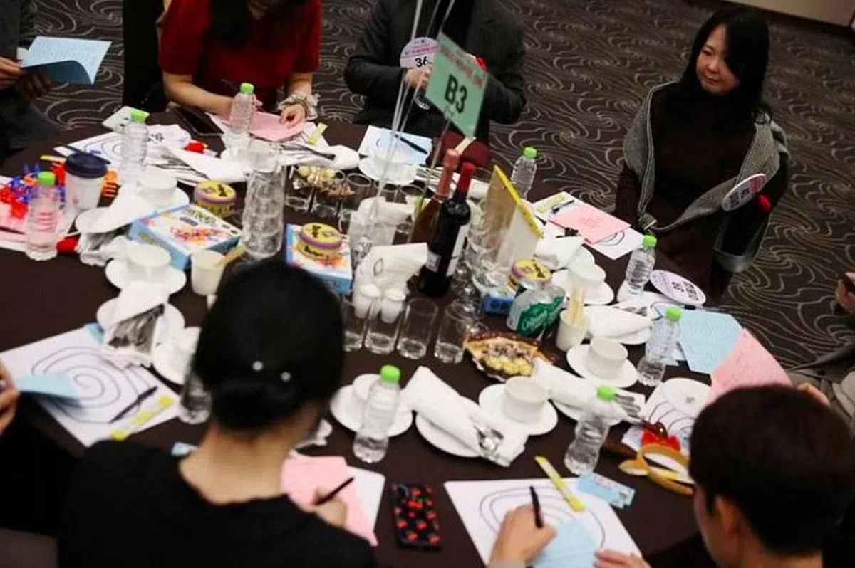 韩国城南市大型相亲会场的圆桌上摆放着红酒和巧克力，参与者通过游戏“破冰”，短时间内就开始与周围的新朋友交流。（路透社）