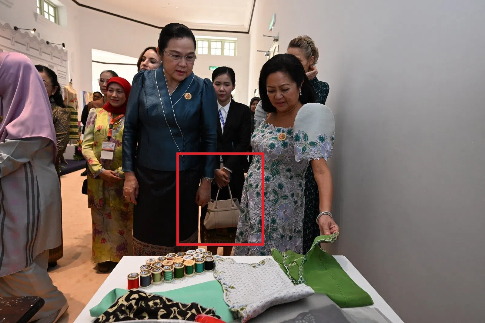 老挝总理夫人万达拉·西潘敦（蓝色上衣者）身后的随行人员协助拎包。