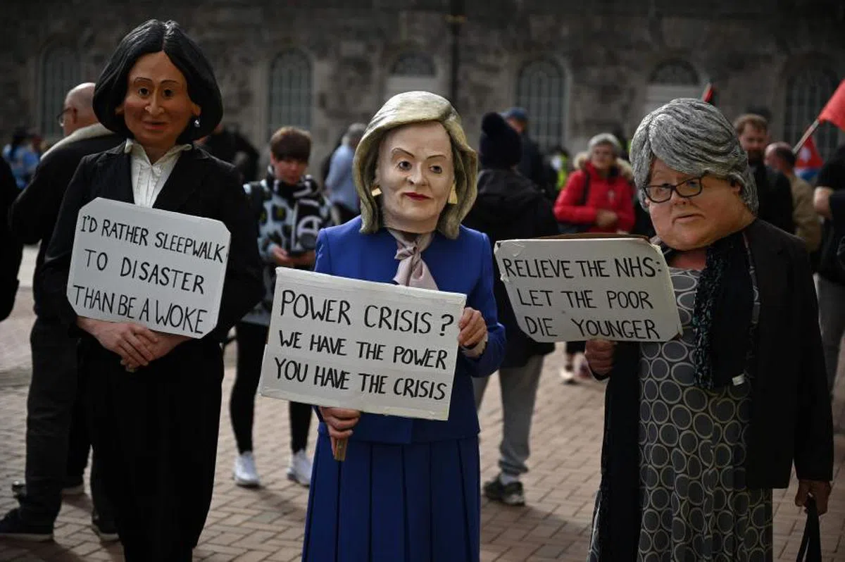 扮成特拉斯（中）等英国政治人物的示威者在反政府示威中手举标语。（法新社）