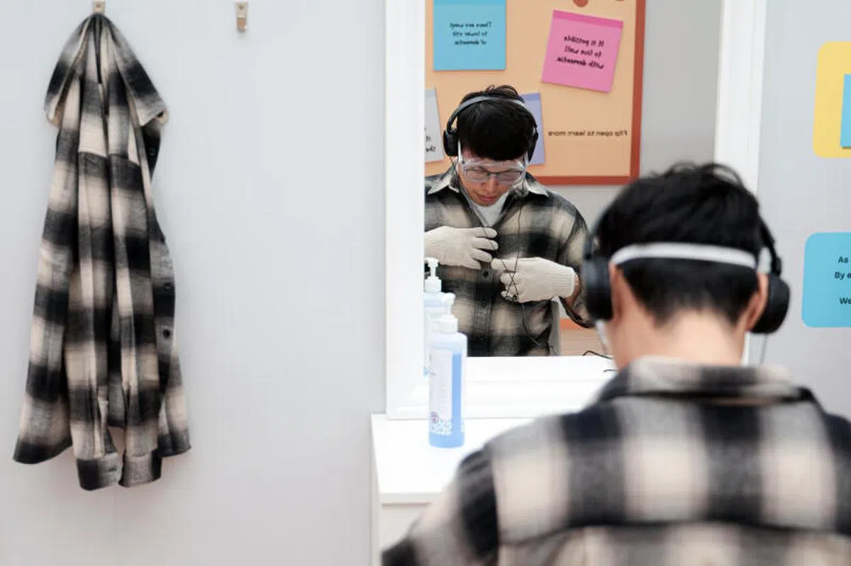 2024年1月国家博物馆二楼望山堂（Glass Atrium）的“失智友善新加坡展”。公众可在套上手套和防护镜后，为自己穿衬衫，切身体会失智症患者每天更换衣服的不易。（联合早报）