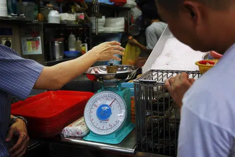 新加坡企业发展局属下的度量衡办公室（Weights and Measures Office）官员正使用一个一公斤重的金属块来检测商用秤的精准度。（海峡时报）