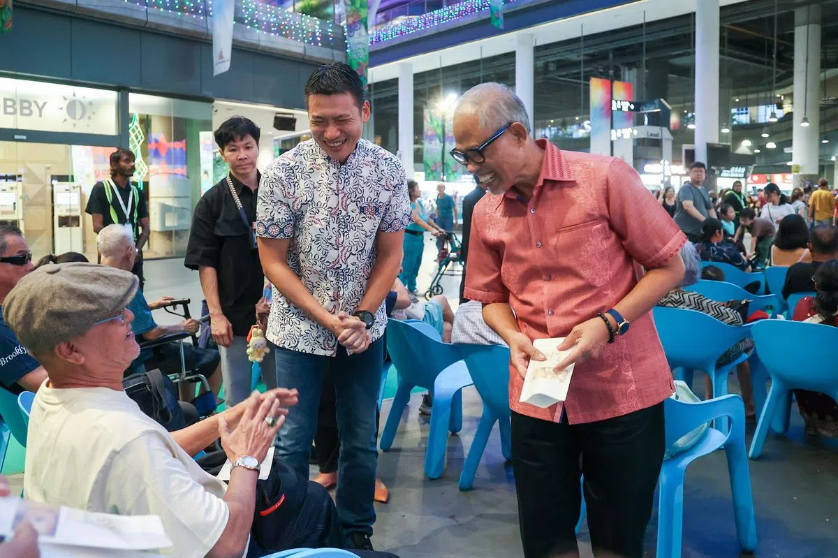 社会及家庭发展部长兼卫生部第二部长马善高（右）和梁振伟在开斋节活动上分发饼干给淡滨尼居民。（联合早报）