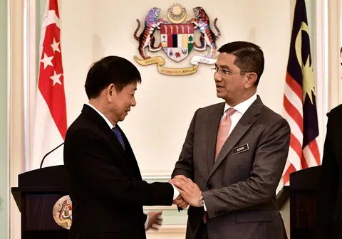  新加坡基础建设统筹部长兼交通部长许文远（左）与马来西亚经济部长阿兹敏在记者会结束后握手言欢。（路透社）