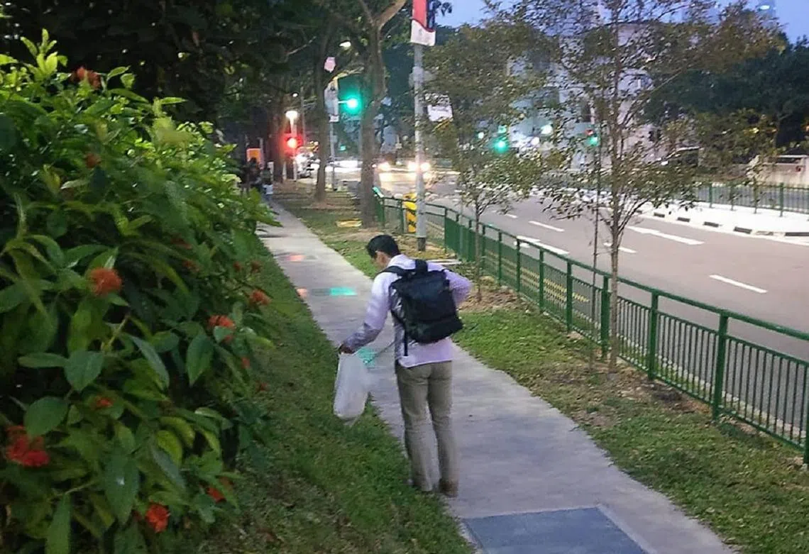 一名穿着卡其色西装裤和长袖白衬衫，看似上班族的中年男子背着黑色双肩包，正在路边弯腰捡垃圾。（Ivan Choong面簿）