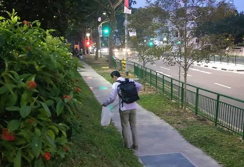一名穿着卡其色西装裤和长袖白衬衫，看似上班族的中年男子背着黑色双肩包，正在路边弯腰捡垃圾。（Ivan Choong面簿）