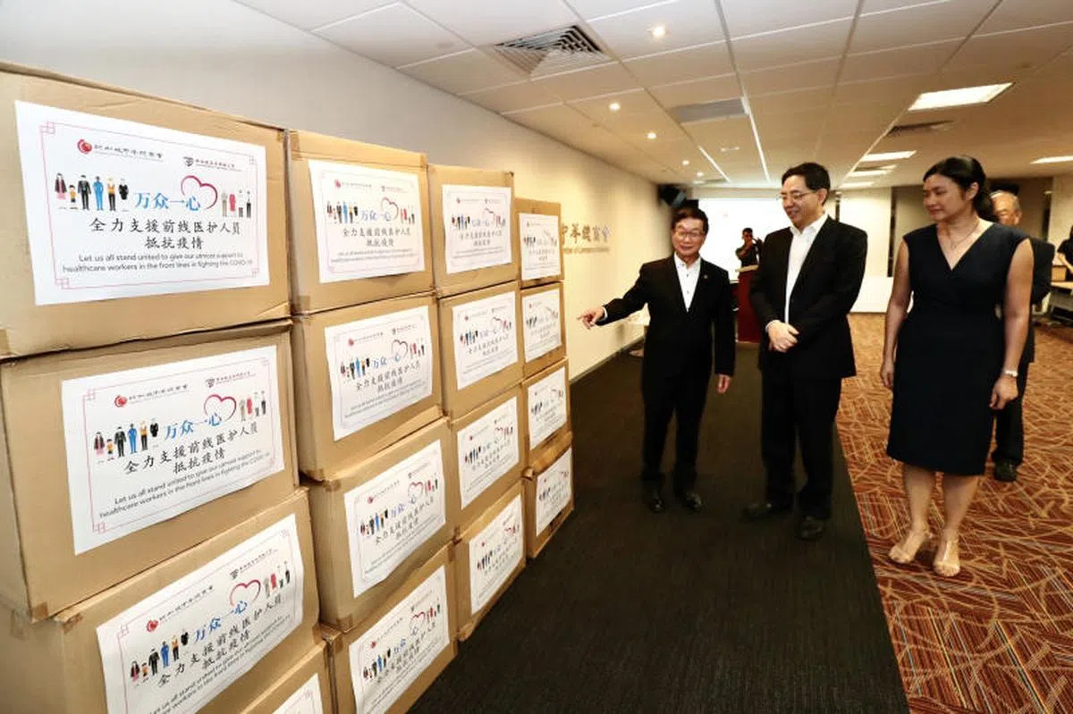  新加坡中华总商会捐赠3800套医疗防护服和1万个医用口罩给本地前线医护人员，另筹款110万新元支援中国社群。2020年2月17日，新加坡中华总商会会长黄山忠（左起）向中国驻新大使洪小勇和卫生部医药总监办公室项目司长陈瑄玲介绍筹集来的捐献物资。（新明日报） 