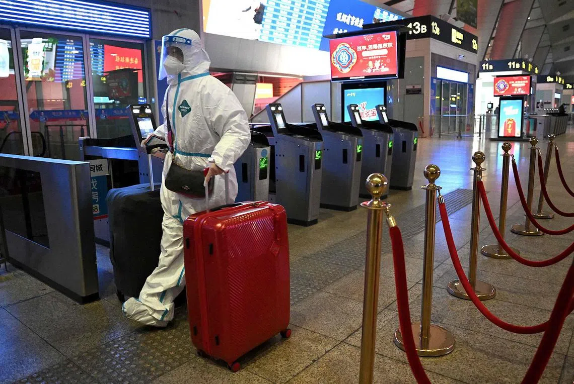 一名穿着个人防护设备的乘客拖着行李抵达北京的一个火车站。（法新社）