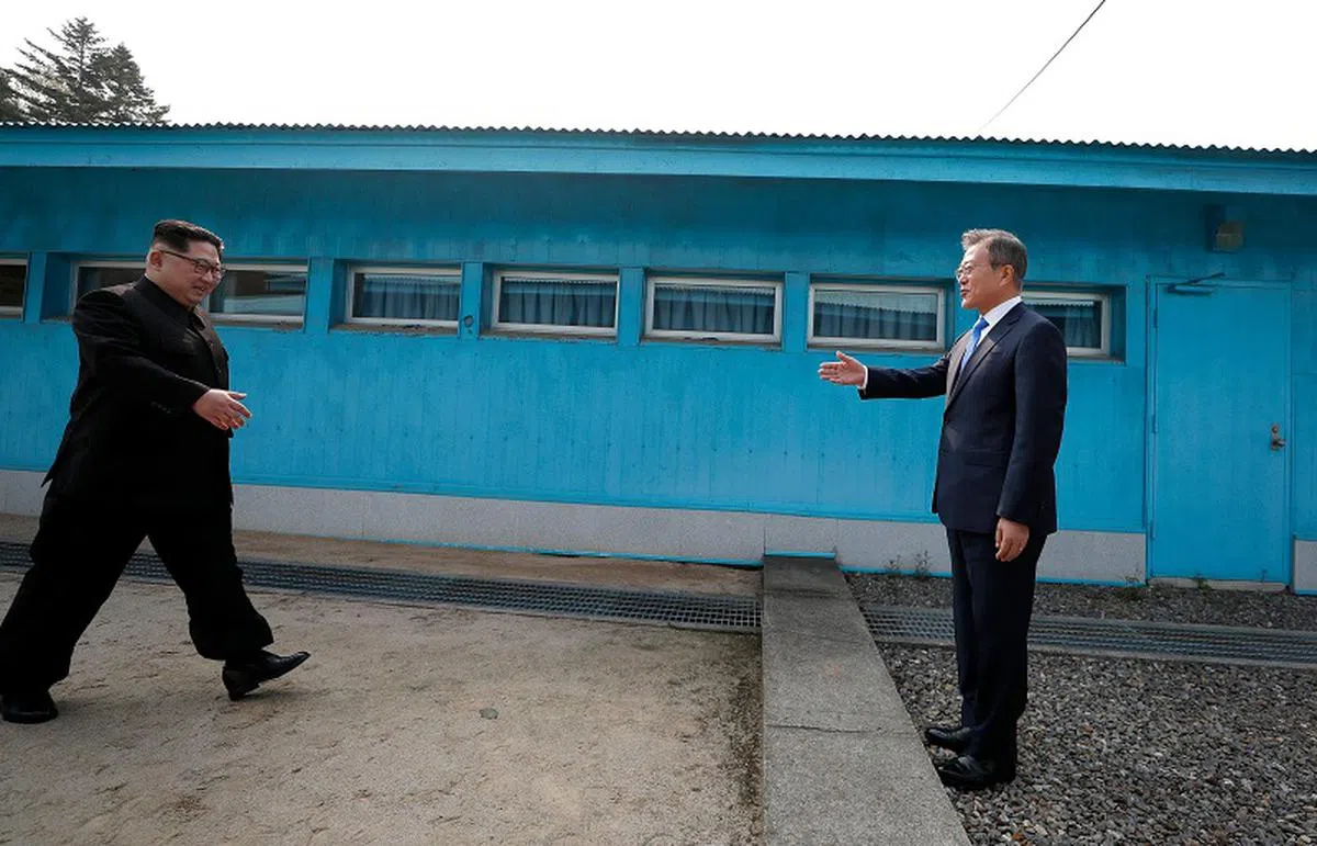  朝鲜最高领导人金正恩在板门店朝方一则的“板门阁”慢慢走近军事分界线，与伸出手的韩国总统文在寅握手。（路透社） 