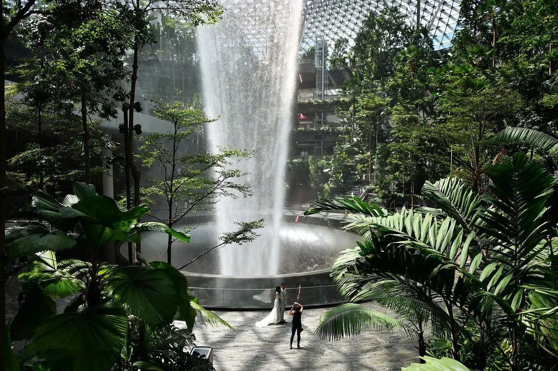 一对新婚夫妇在星耀樟宜的雨漩涡前留影。（海峡时报）