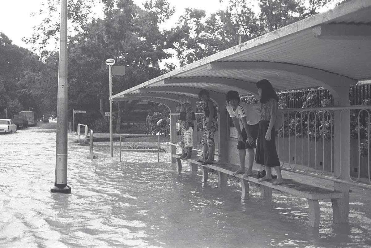 1977年，马路淹水时，到巴士站躲一躲准没错。（海峡时报）