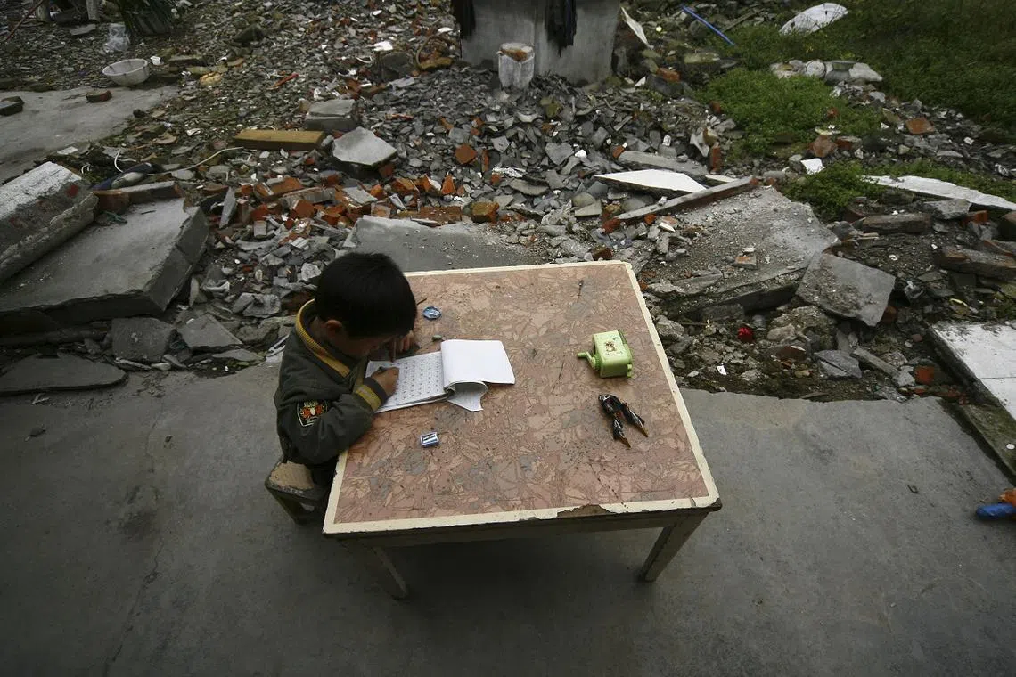 中国汶川地震一周年之际，一名学生在四川灾区的废墟中埋头写作业。（法新社） 