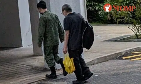 Stomper J shared a photo of the man in camouflage walking in front of an elderly man carrying a black backpack and a yellow plastic bag in a Housing Board estate.