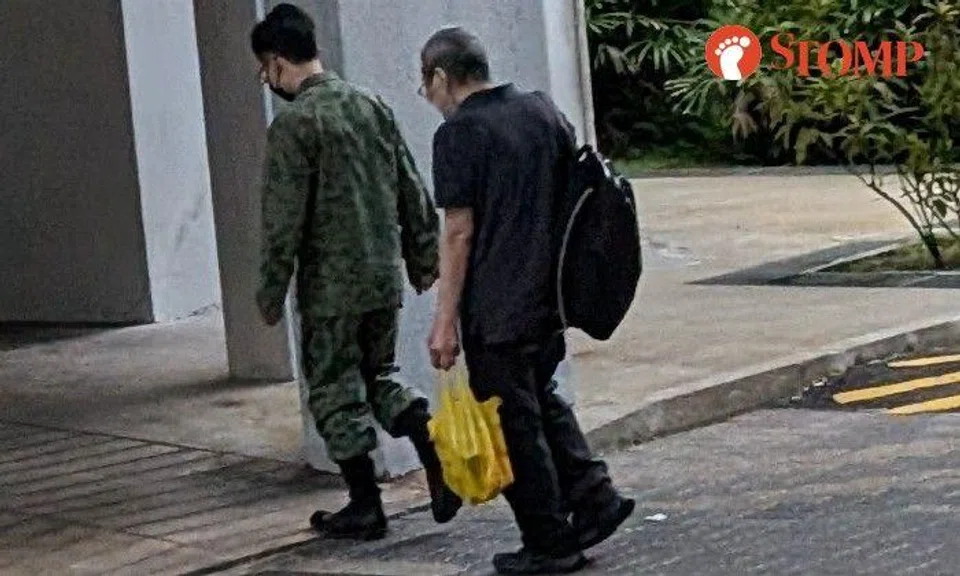 Stomper J shared a photo of the man in camouflage walking in front of an elderly man carrying a black backpack and a yellow plastic bag in a Housing Board estate.