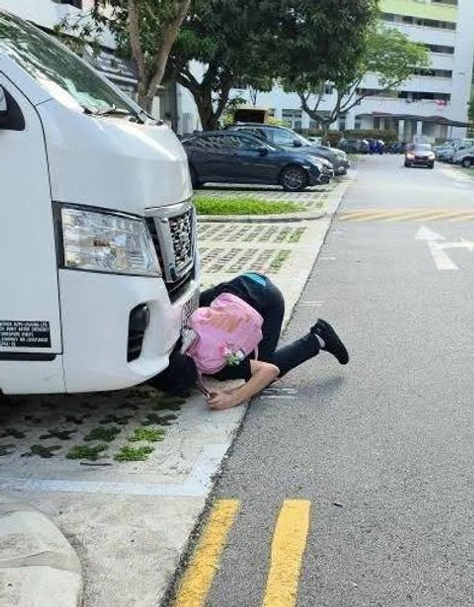 Man crouching and peering under a van in a carpark, allegedly trying to splash water to lure a cat out.