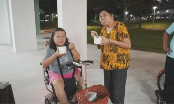 Two elderly women holding soup pose for a photo.