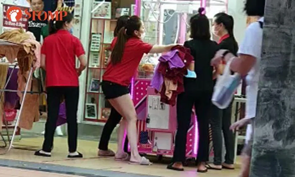 Women lift and shake claw machine outside Toa Payoh salon to get toys