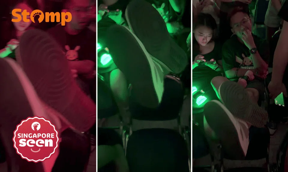 Audience member props feet up on back of another concertgoer's seat