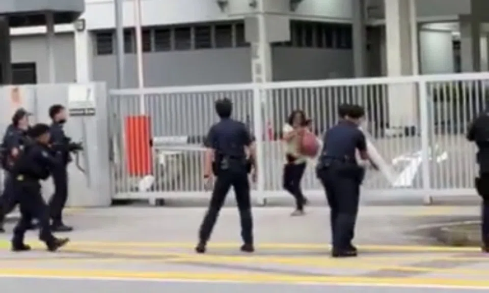 In videos posted online, the woman - who was wearing a green top, black pants and with a red bag looped around her waist - was seen surrounded by at least 10 police officers outside St Hilda's Secondary School.