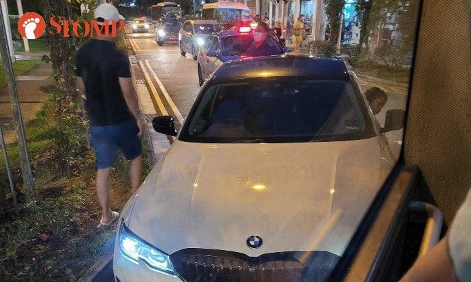 The photo shows a man wearing a white cap standing next to the BMW facing a man wearing a mask. 