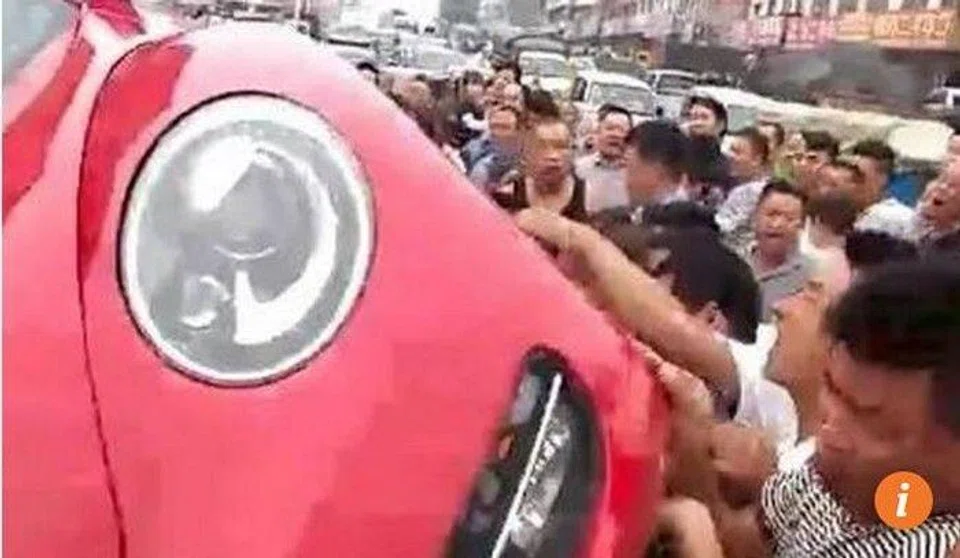 Enraged crowd tip over car in China after driver slaps jaywalker