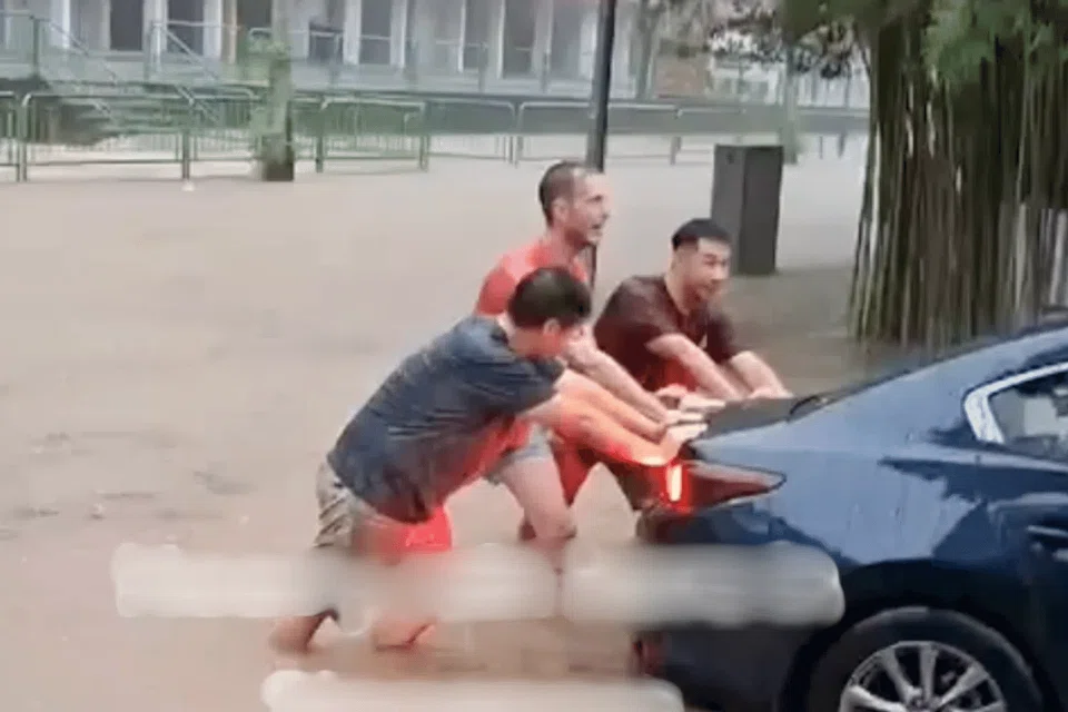 Three men can be seen pushing the car out of the ankle-deep water while drenched in the rain. 