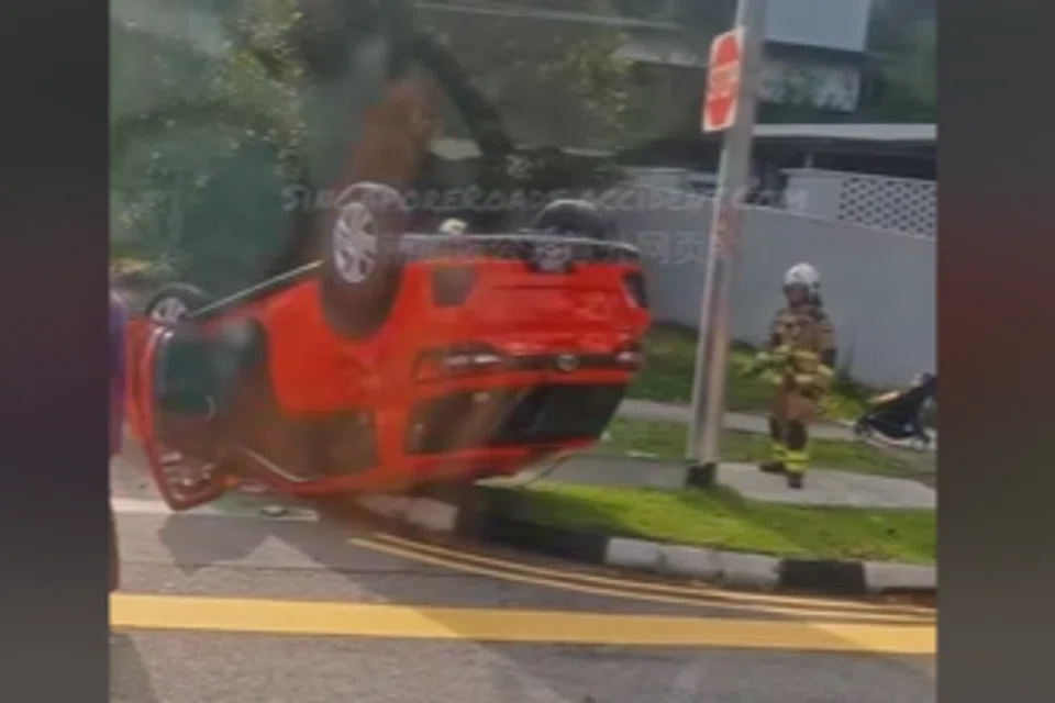 Video footage shows a red car overturned on a pavement. 