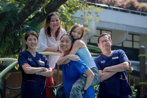 Sara Grace Kueh, 17, (piggybacked by older sister, Isabelle Joy Kueh, 26, a staff nurse at NUH) with (from left) Dr Frances Yeap, her oncologist; Mrs Esther Kueh, 52, her mother; and Adjunct Professor Mark Puhaindranon, her surgeon. 