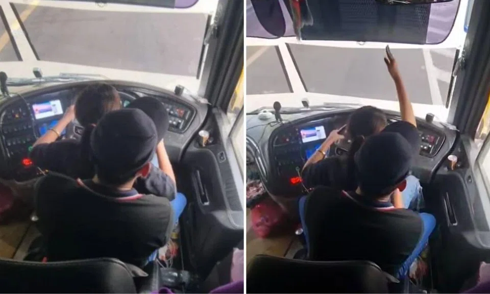 woman sits on bus driver’s lap with hands on steering wheel 