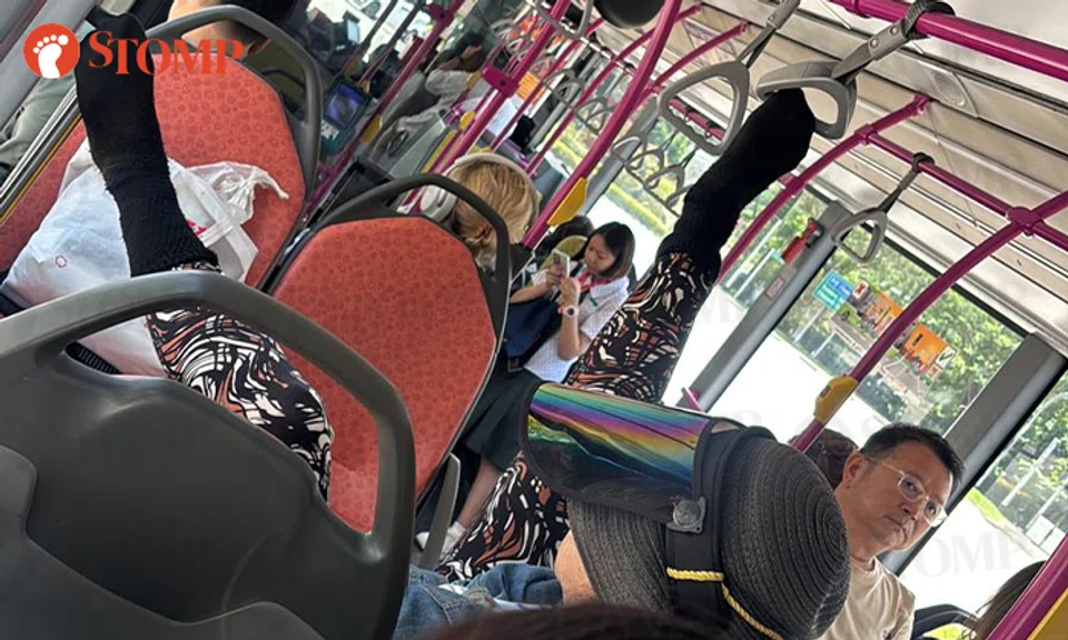 woman puts feet up on handrail in bus