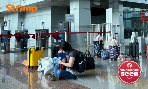Travellers leave luggage unattended to reserve their spot in the queue, a woman sitting in the centre of the image attends to her own belongings